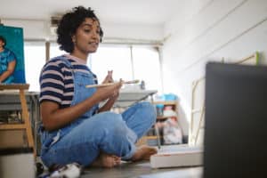 Lady artist in overalls taking online art class.