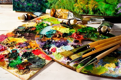 palette with paintbrushes and canvas paintings. Learn art online.