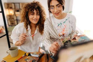 Young female artists paint in their studio as friends online.