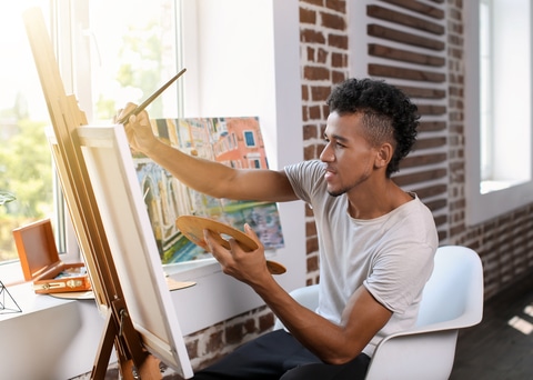 Young man painting in front of a window. How lighting affects your artwork.
