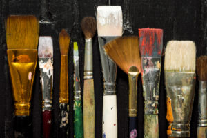 Artist`s tools, brushes in paint are in a row on a black wooden background. Art Supplies You Can’t Live Without - Yarnell School