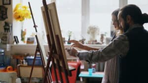 Skilled artist providing art criticism to young artist painting in an art studio. Yarnell School