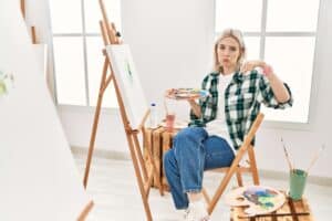 Young artist woman painting on canvas at art studio pointing down looking sad and upset, indicating direction with fingers, unhappy and depressed. 5 Things to Avoid When Painting with Acrylics - Yarnell School Online.