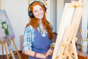 Smiling woman artist painting on canvas and listening to painting lessons or music. Unlocking the Art of Portrait Painting - Yarnell School Online
